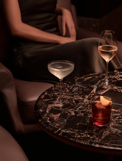 Cocktail service at Aman Nai Lert Bangkok's lounge, with a server pouring a drink beside a marble table.