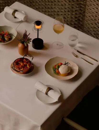 アマン ナイラート バンコクのレストランで、白いテーブルに配置された食事風景。皿とグラスが整然と並び、前菜とワインが準備されている。