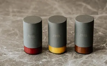 Three cylindrical jam jars with concrete-effect lids and red, yellow, and brown bands at Aman Nai Lert Bangkok.