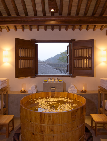 Circular wooden bathtub in a spa suite at Amanfayun with mountain views through open shutters.