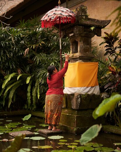 Flower offering ceremony at Amandari, Bali, with red and gold silk cloth arrangement amongst tropical foliage.