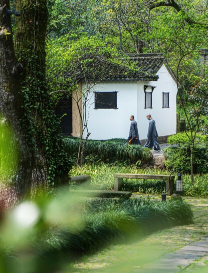 Monk walking through lush gardens at Amanfayun, China.