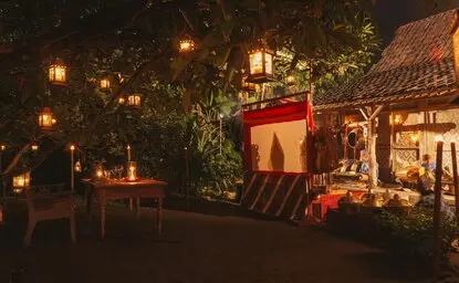 Candlelit Javanese wayang dinner setup at Amanjiwo, with traditional puppet theatre backdrop and lanterns glowing among tropical foliage.