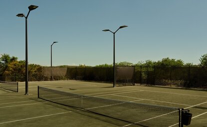 Terrain de tennis à Amanyara avec filet et lampadaires, entouré de végétation tropicale.