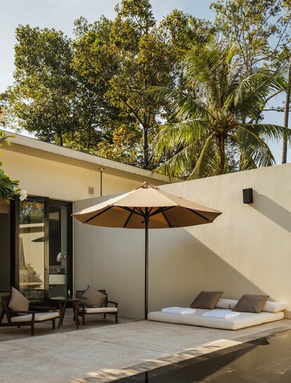 Pool Suite outdoor seating area at Amansara, with parasol and garden courtyard views.