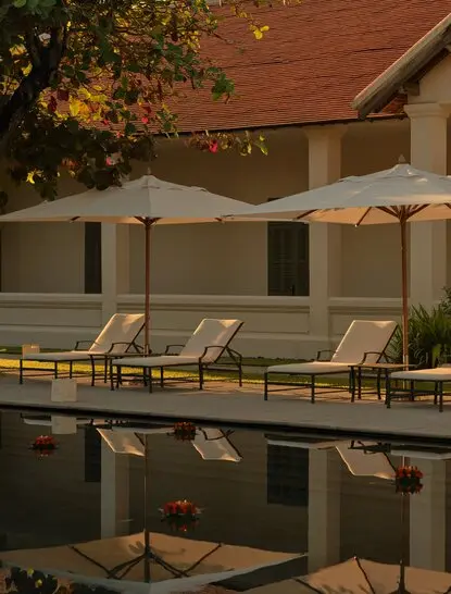 Loy Krathong ceremony at Amantaka's pool terrace at dusk, with cream sun loungers and umbrellas reflected in still water.