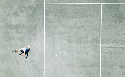Aerial view of tennis court at Amanyara with players on pale grey surface.