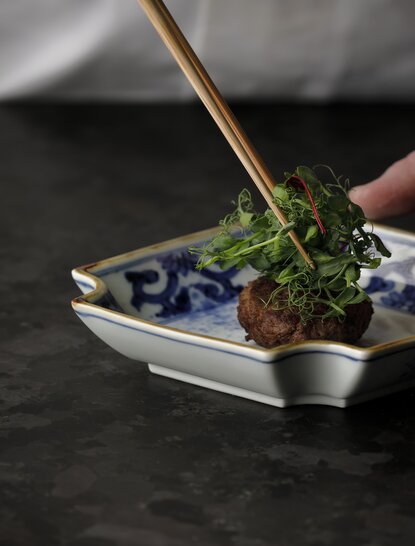 Chopsticks lifting beef and foliage from a ceramic dish at Aman Kyoto's Hirai kaiseki dining experience.