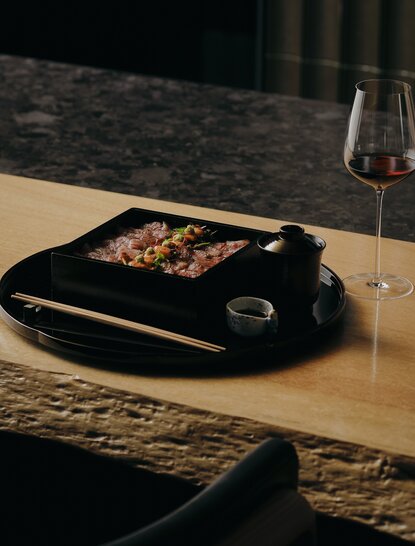 アマン京都のレストランで提供される和牛を使用した懐石料理。木製カウンターの上に黒い器に盛られた料理。