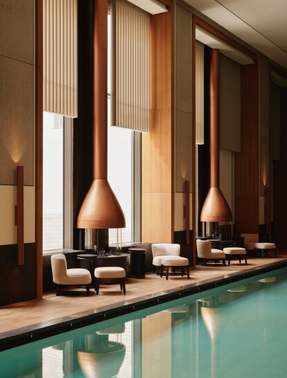 Indoor swimming pool at Aman New York with spa and wellness facilities, featuring warm wood accents and modern architecture.
