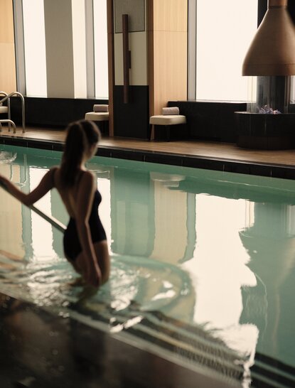 Spa guest entering a serene swimming pool at Aman New York, with natural light reflecting off the water.
