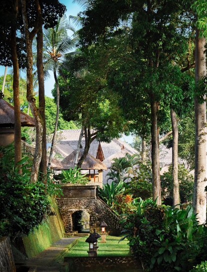 Amandari resort garden with tall trees, manicured lawns, and stone pathways winding through tropical vegetation.