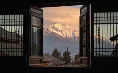 大研安缦度假村内，透过传统木制窗框眺望远处雪山的景观。