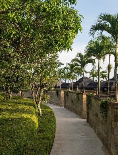 Pathway lined with lush greenery and palm trees at Amanjiwo resort, Indonesia.
