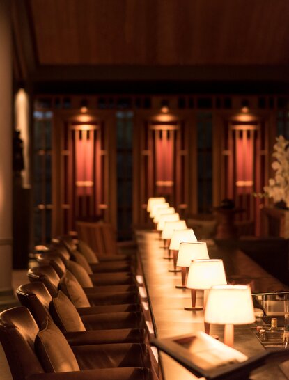 Amanoi's bar dining room with a long table set with candles and place settings, backed by warm-glowing wooden panels.