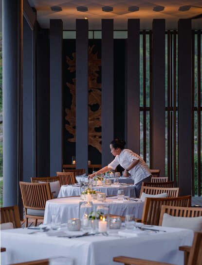 Amanoi's Beach Club Restaurant dining room with wooden chairs, white tablecloths, and vertical timber screens filtering natural light.