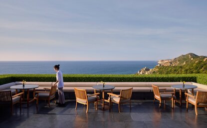 Amanoi's main restaurant terrace overlooking the sea, with wooden dining tables and a solitary figure gazing at the coastline.