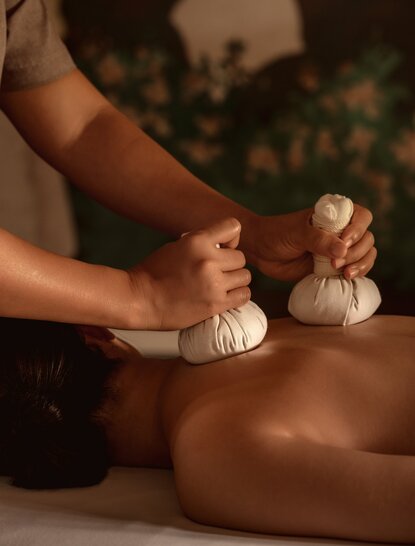 Therapist applying herbal compress to guest's back during spa treatment at Amanoi, Vietnam.