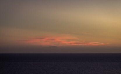 Sunset over the horizon at Amanvari, Mexico, with warm amber and rose tones reflecting across a darkening landscape.