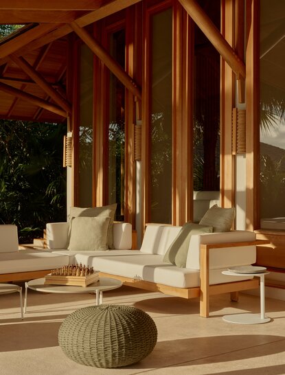 Outside living area at Amanyara with wooden pavilion, cream seating, and woven poufs overlooking tropical grounds.