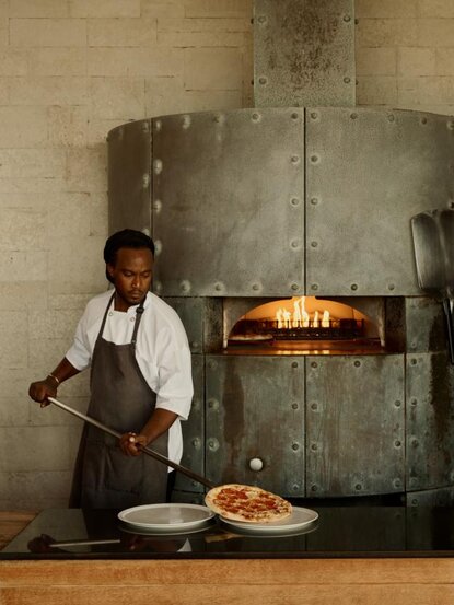 Chef preparing food at Amanyara resort's beach club restaurant, wood-fired oven in background.