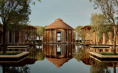 Amanyara's main resort reflected in still water, with wooden pavilions and palm trees at dusk.