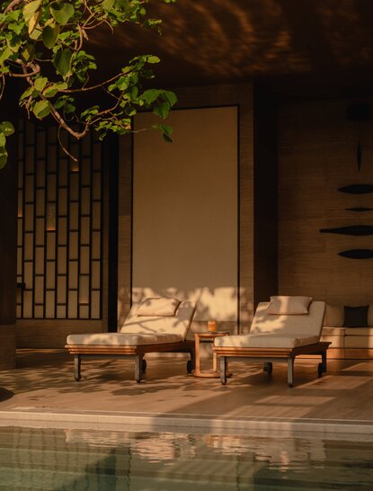 Evening view of the pool pavilion at Aman Nai Lert Bangkok, with cream armchairs and soft lighting by the water's edge.