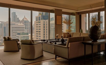 Aman Suite at Aman Nai Lert Bangkok with floor-to-ceiling windows overlooking the city skyline, furnished with neutral-toned seating and a work desk.