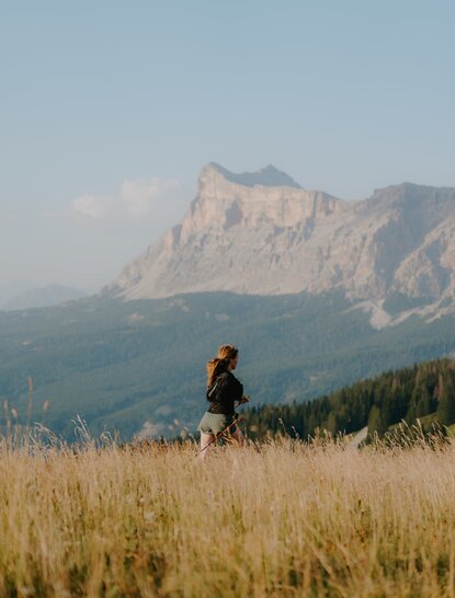 Skyrunner in golden grassland overlooking alpine mountains at Aman Rosa Alpina resort, Italy.