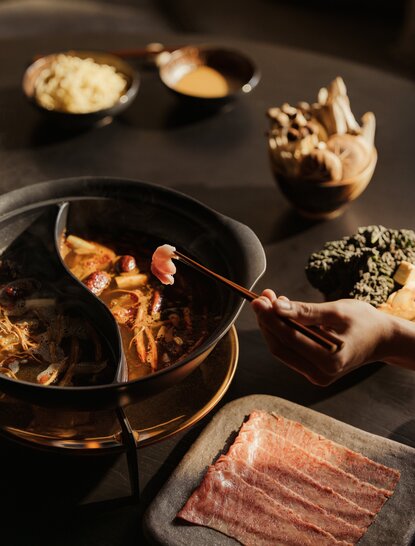 Aman Rosa Alpina: chef's hands preparing Italian cuisine in a dark kitchen setting with ingredients and cookware.