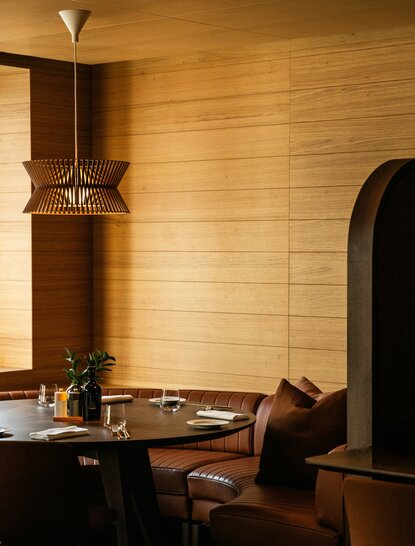 The Grill dining room at Aman Rosa Alpina, with warm wood panelling, a suspended brass light fixture, and a table set for dining.
