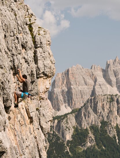 Rock climber scaling pale limestone cliff with jagged Alpine peaks beyond at Aman Rosa Alpina.