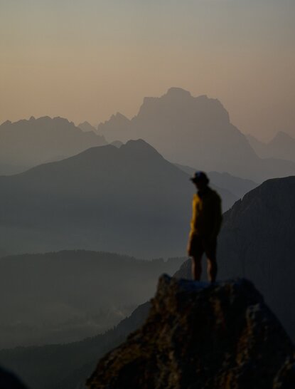 Silhouetted figure standing on a mountain outcrop overlooking misty Alpine valleys at Aman Rosa Alpina.