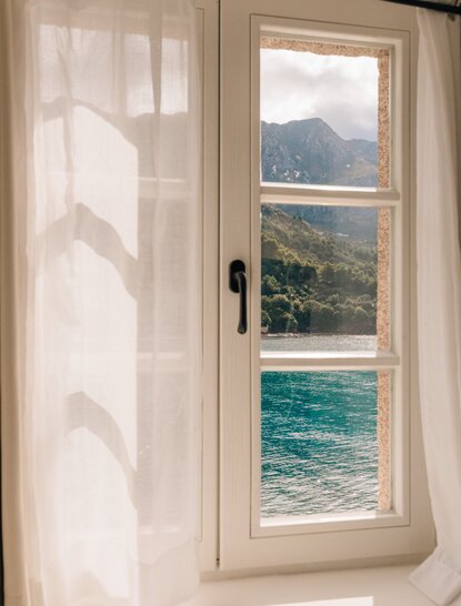 Deluxe cottage window framing Adriatic Sea and coastal mountain views at Aman Sveti Stefan, Montenegro.
