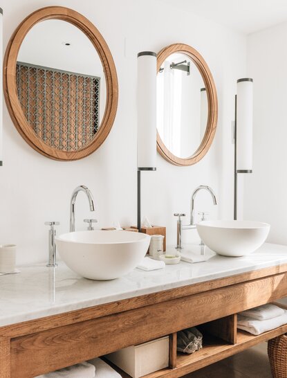 Deluxe cottage bathroom at Aman Sveti Stefan with wooden vanity, dual vessel sinks, and woven mirrors.