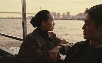 Two guests converse on a Sumida River cruise at Aman Tokyo, with the city skyline visible across the water.