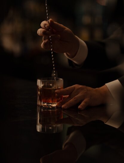 Cocktail being prepared at The Lounge, Aman Tokyo hotel, with amber liquid being poured into a glass.