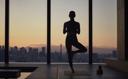 Silhouette d'une personne pratiquant le yoga au coucher du soleil face à la skyline de Tokyo, Aman Tokyo.
