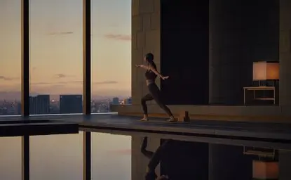 Silhouette of a person practising yoga at Aman Tokyo, with Tokyo's skyline visible through floor-to-ceiling windows at dusk.