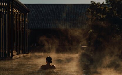 Person soaking in a steaming onsen at Amanemu, Japan, with wooden architecture framing the scene.
