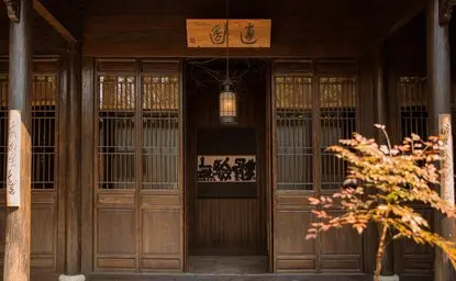 Wooden entrance doors at Amanfayun with illuminated golden tree and traditional Chinese characters above doorway.