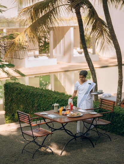 Breakfast table set on the garden terrace at Amangalla, with soft morning light filtering through palm fronds.