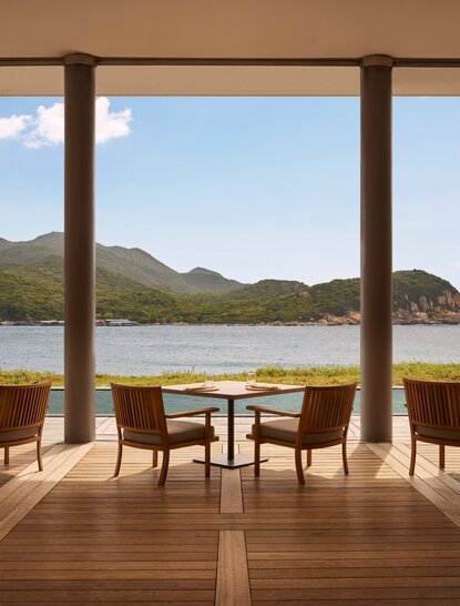 Amanoi beach club restaurant with wooden deck seating overlooking coastal landscape and mountains.