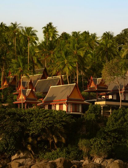 Aerial view of Amanpuri's watersports pavilion nestled amongst tropical palms at golden hour in Thailand.