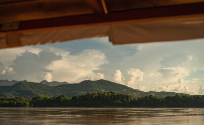 Mekong River sunset view from Amantaka, with distant mountains and clouded sky reflected in calm waters.