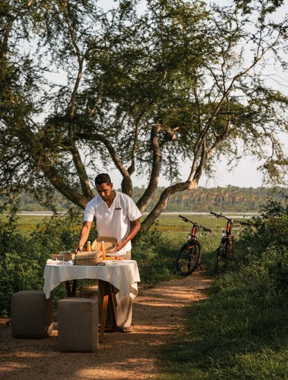游客在斯里兰卡安缦蔚澜度假村骑行体验中驾驶摩托车，穿过树木繁茂的乡村路径。