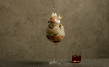 Citrus parfait served in a tall glass at Aman Tokyo's lounge, with a small glass of red liquid beside it.