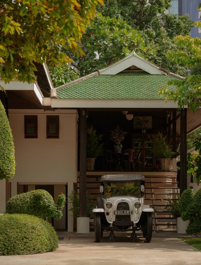 Vintage car parked beneath a covered garage at Aman Nai Lert Bangkok, surrounded by manicured greenery.