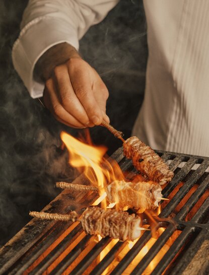 Chef grilling at Aman Venice, flames rising from food on grill grates.