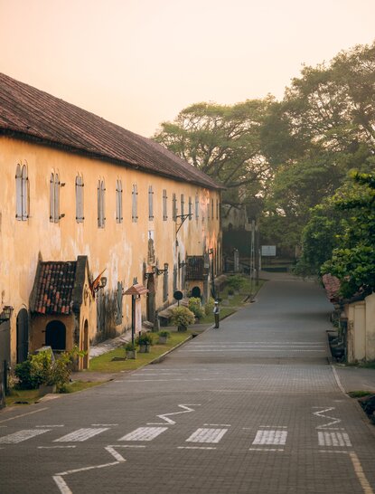 Colonial-era yellow building at Amangalla in Galle Fort, Sri Lanka, with tree-lined pathway.
